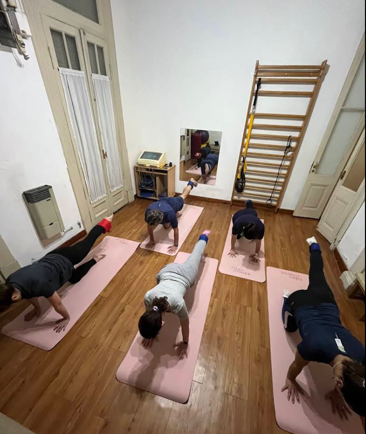 Clase grupal de mat con cinco alumnos haciendo plancha en el estudio